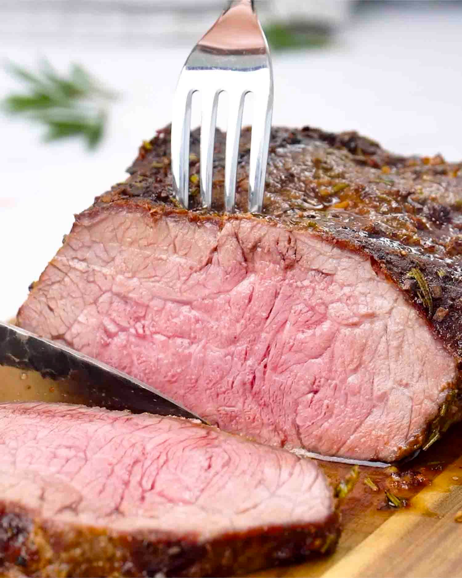 a roast beef made in the air fryer sliced on a cutting board.