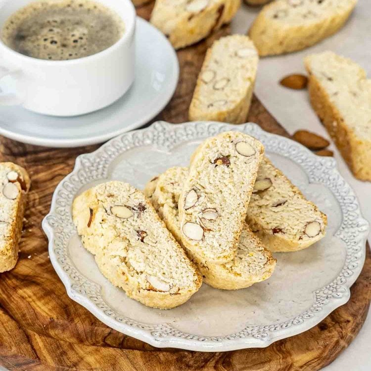 almond biscotti with a cup of coffee on a cutting board.