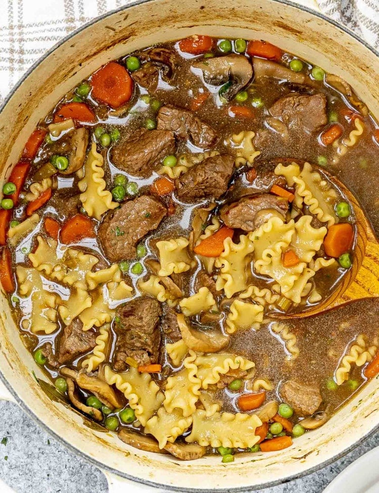 fresh beef noodle soup in a Dutch oven with a wooden ladle inside.