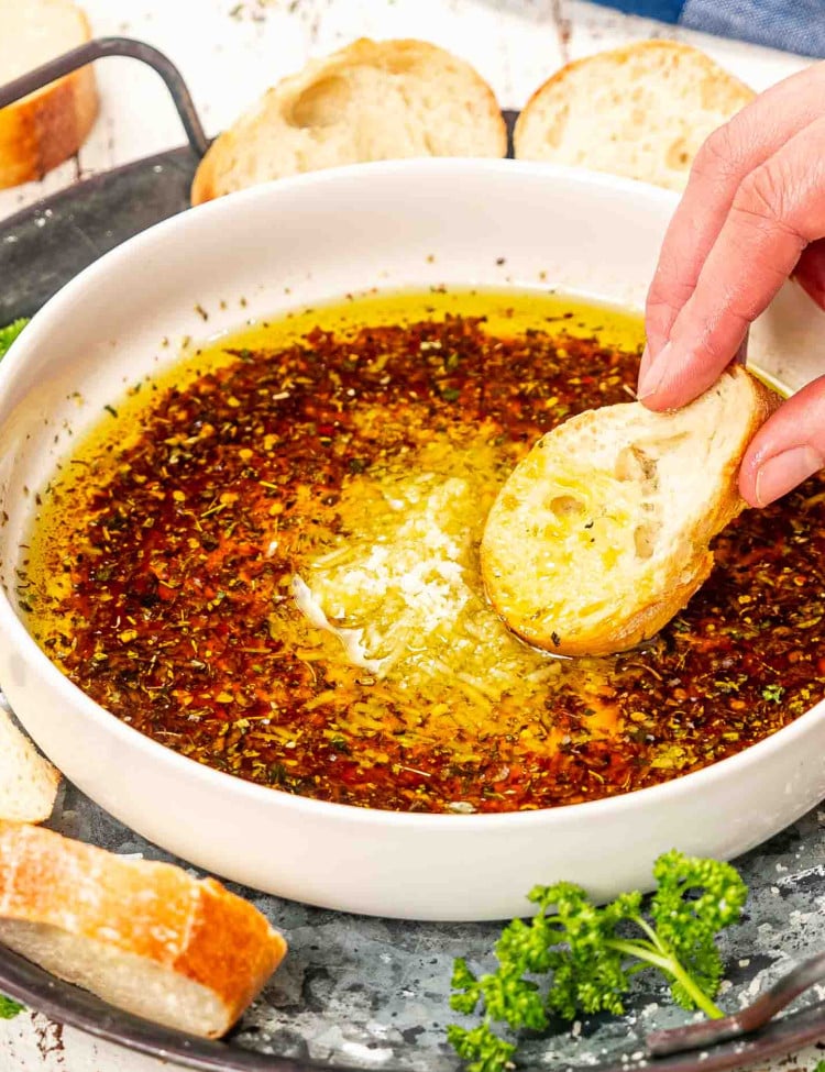 a hand dipping a piece of baguette in a bowl with bread dipping oil.