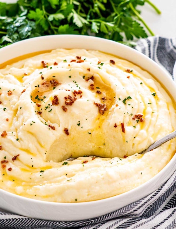 brown butter mashed potatoes in a big white bowl with a serving spoon inside.