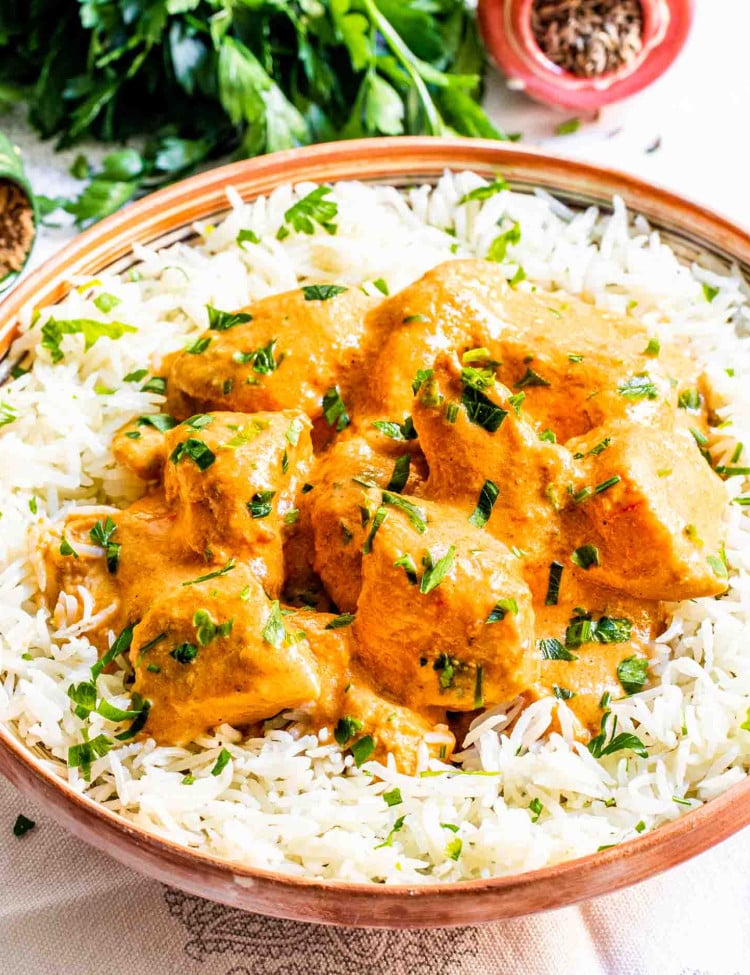 butter chicken over a bed of rice in a plate garnished with cilantro.