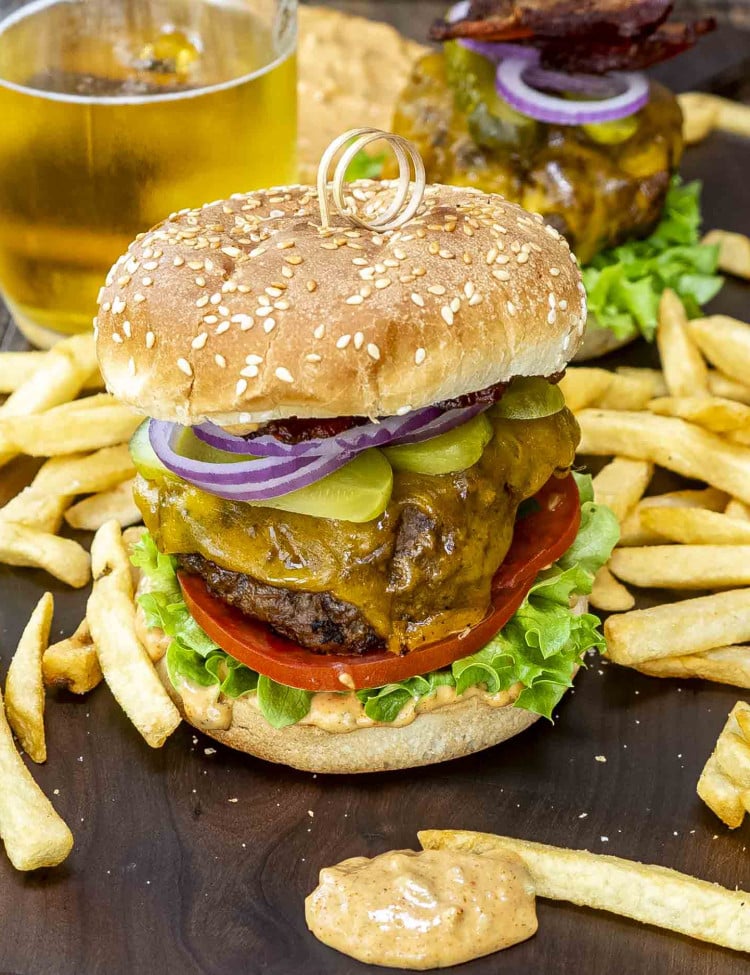 a delicious cheeseburger with secret sauce on a cutting board surrounded by french fries.