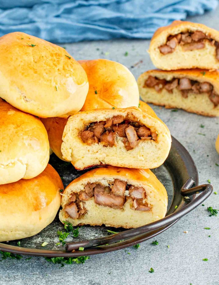 A close-up of Chinese Style Meat Buns, also known as Char Siu Bao, displayed on a plate. The buns are golden brown with a shiny glaze, and one bun is cut open to reveal a juicy, well-seasoned pork filling inside.