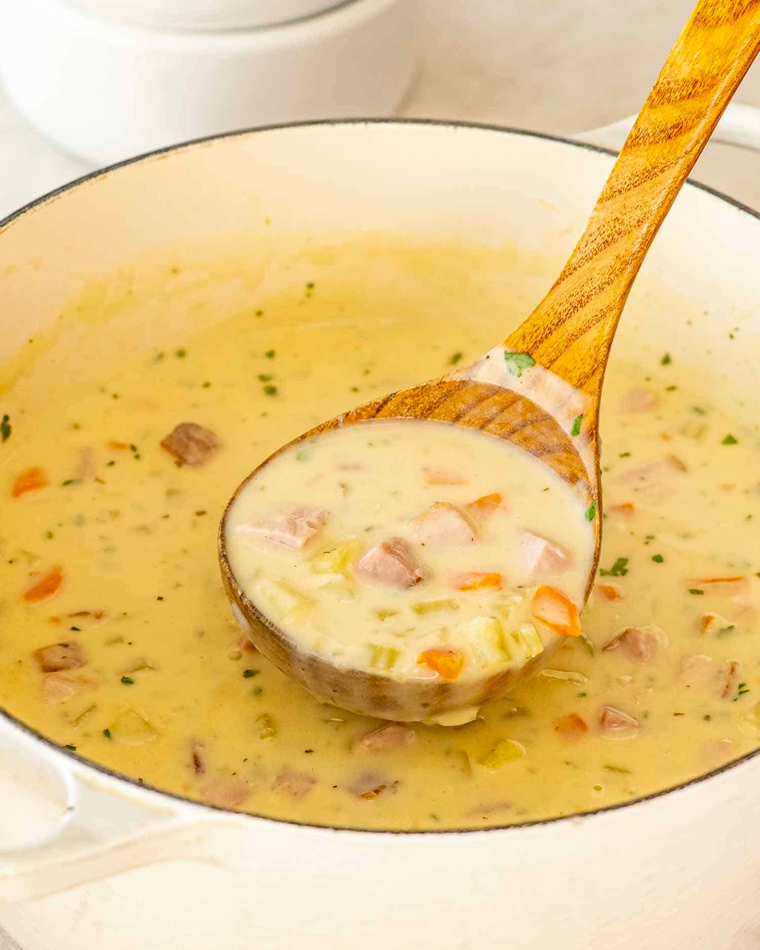 freshly made ham and potato soup in a beige dutch oven.