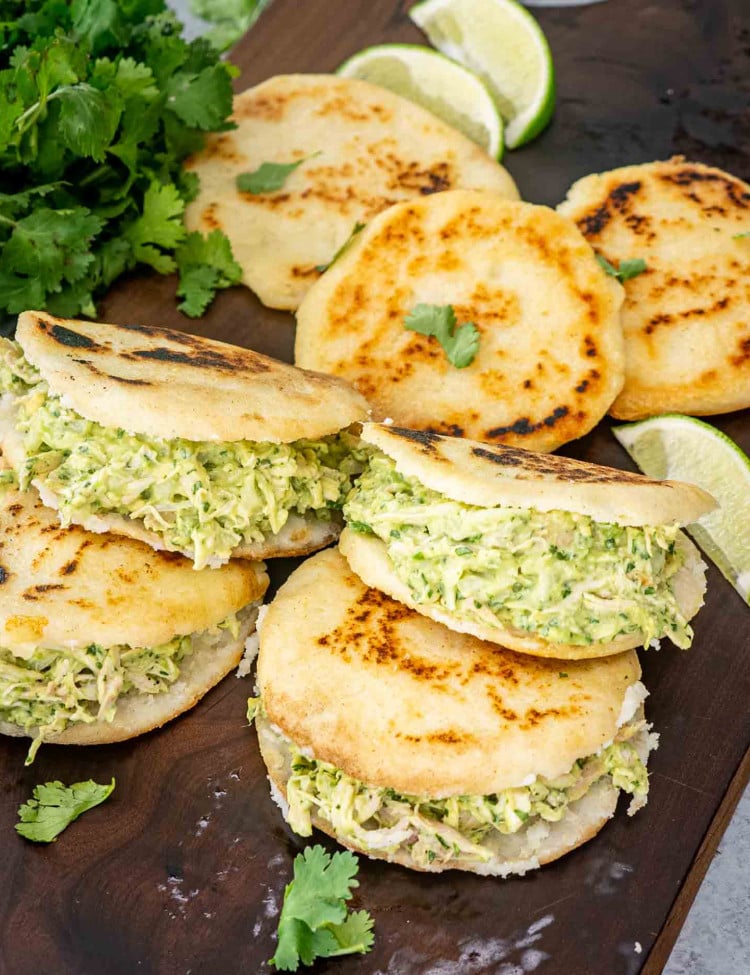 a few arepas on a cutting board stuffed with avocado chicken salad.