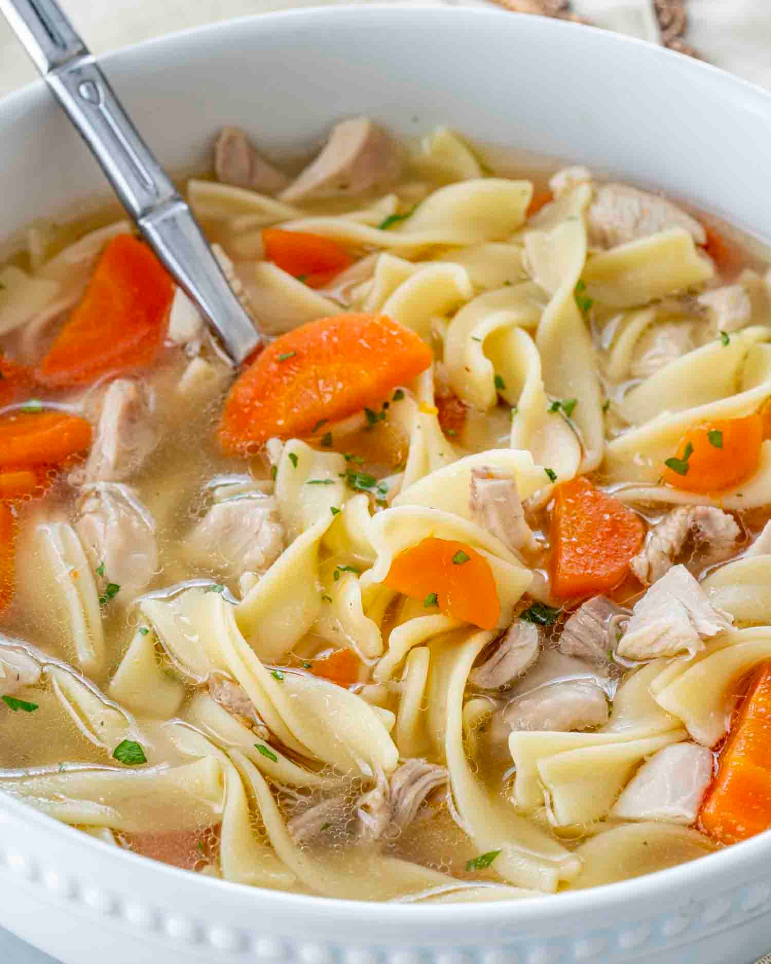 a serving of leftover turkey noodle soup in a white bowl.