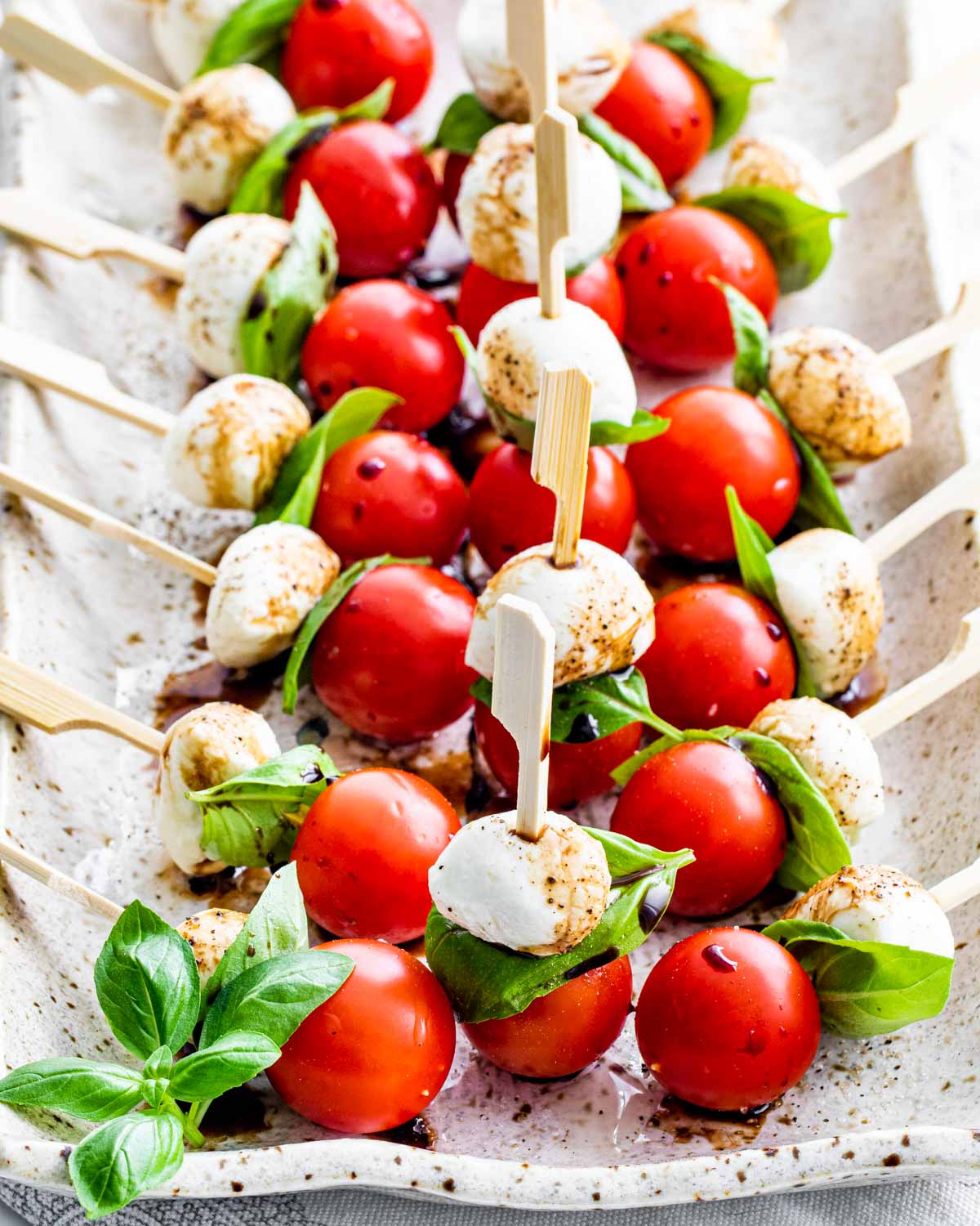 caprese salad bites on a serving platter drizzled with balsamic reduction