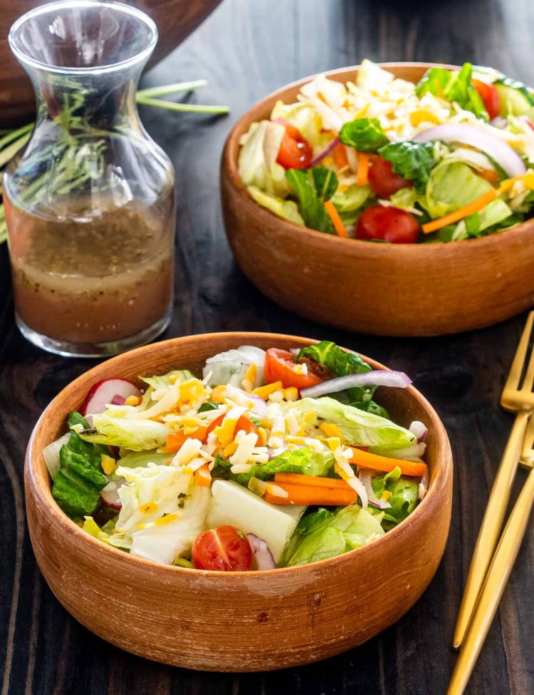 two bowls with tossed salad and salad dressing in a jar.