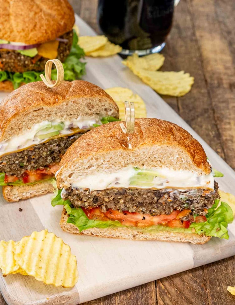 a veggie burger cut in half on a cutting board surrounded by potato chips.